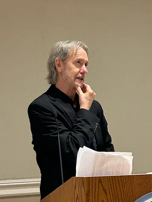 A male speaker strokes his chin during a talk behind a lectern