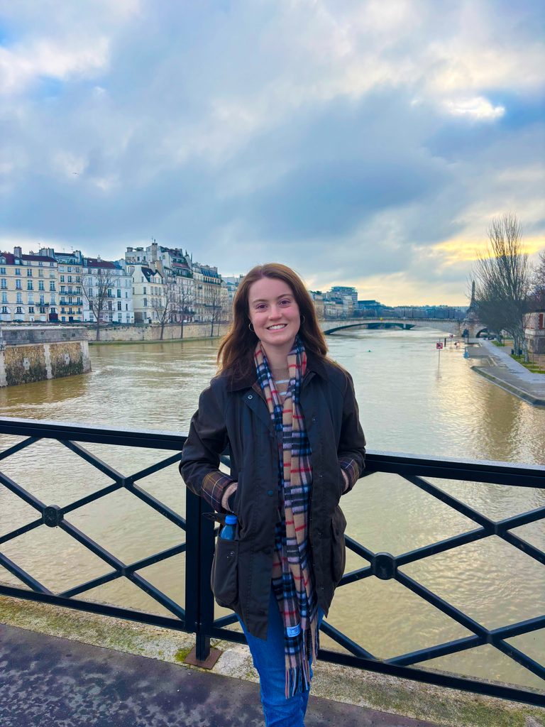 Kate Faulkner stands on a bride overlooking a river and city below.