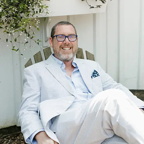 A photo of a man in a white suit sitting in an outdoor chair