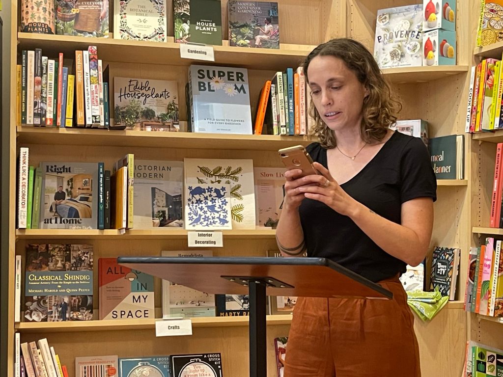 Speaker standing at a podium in a bookstore with shelves behind her